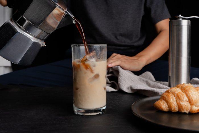 An image of a person pouring coffee into a glass filled with ice cubes