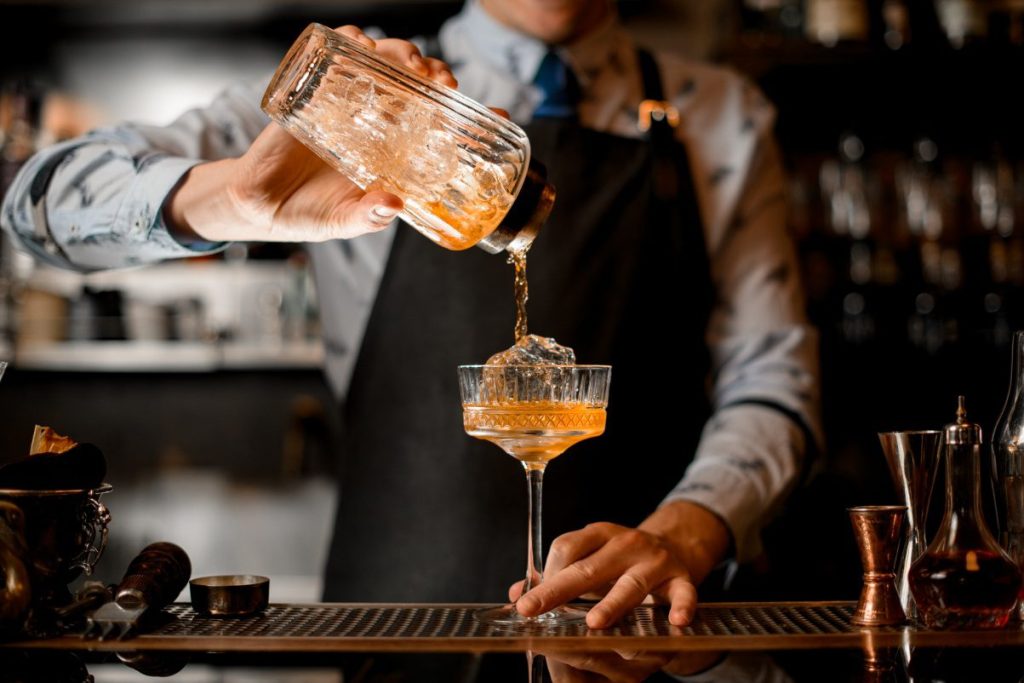 An image of a bartender pouring a drink in a glass with ice